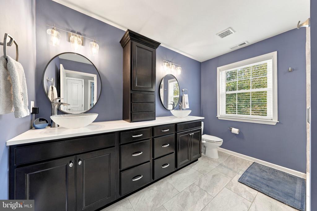 Bathroom with a long dark double vanity, vessel sinks, and a window overlooking greenery.