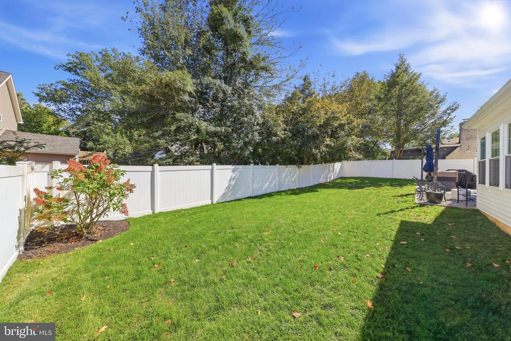 Fenced backyard with a broad green lawn, patio seating, and mature trees.