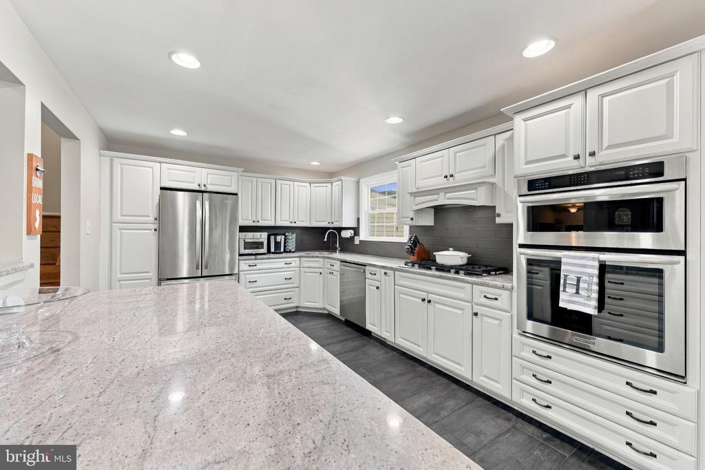 Kitchen with white cabinetry, stainless steel appliances, and a broad stone island.