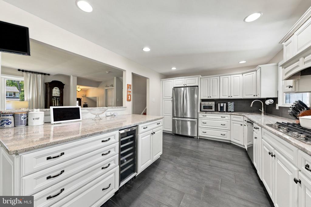 White kitchen with a large stone island, stainless steel refrigerator, and gray tile floor.