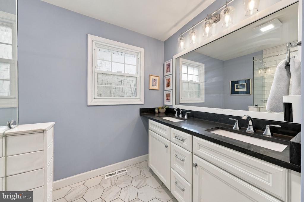 Bathroom with a long double-sink vanity, black countertops, and white hexagonal floor tile.
