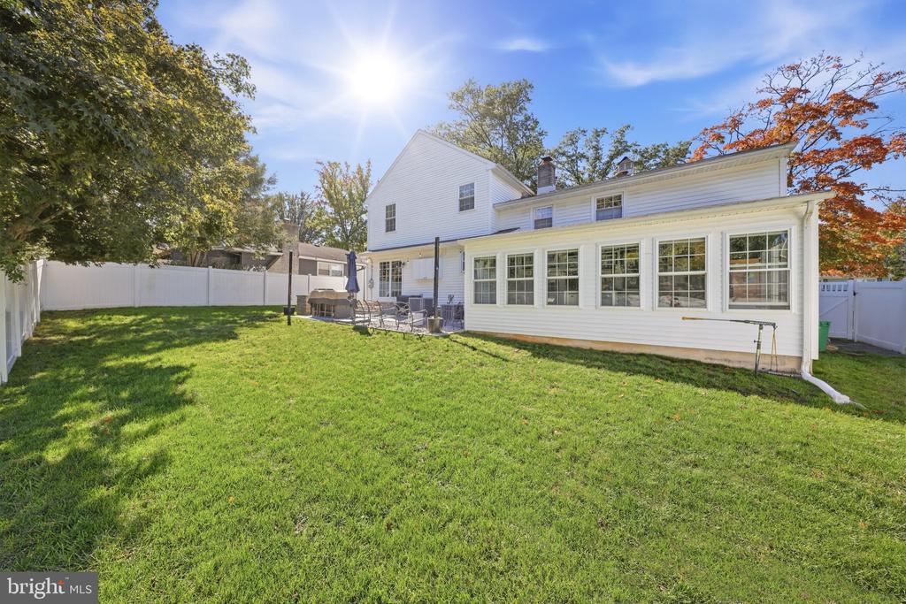 Rear of a white-sided house with a long sunroom, fenced lawn, and patio.