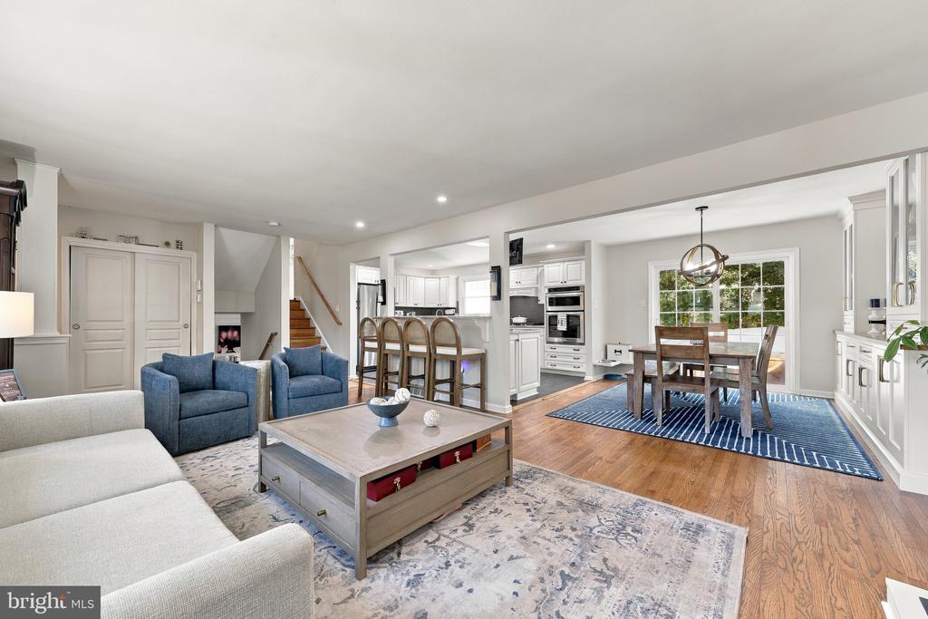 Open living room, kitchen, and dining area with blue armchairs, wood floors, and a dining table by large windows.