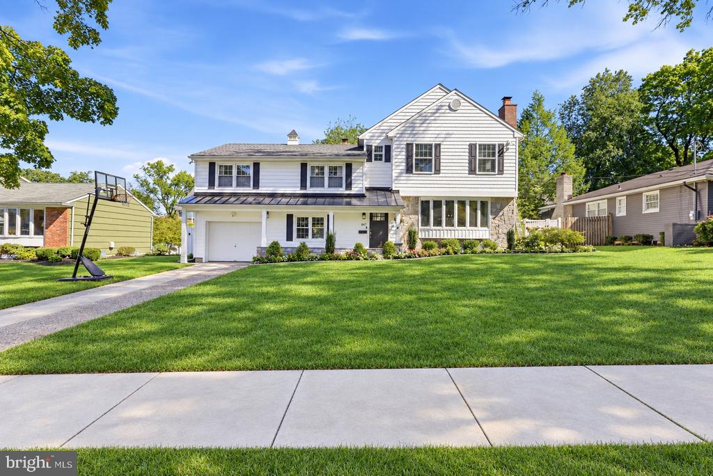 White two-story house with stone accents, a broad green lawn, and a basketball hoop by the driveway.