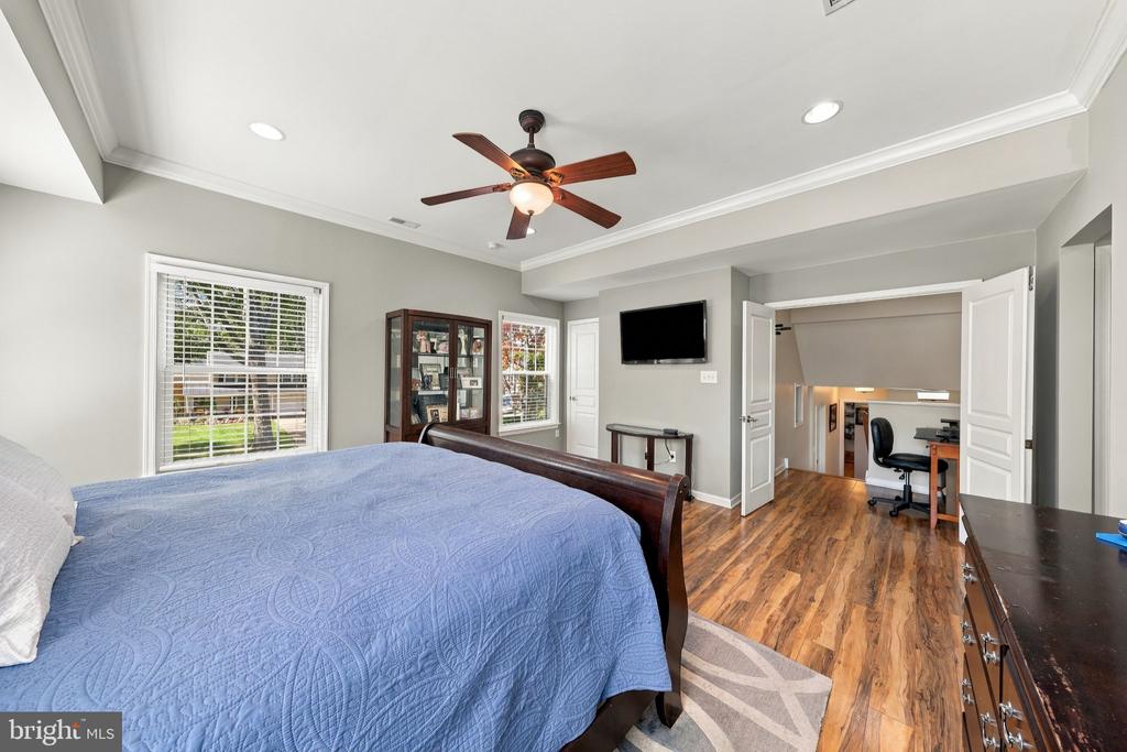 Bedroom with a blue-covered bed, ceiling fan, and doorway to a lower-level office.