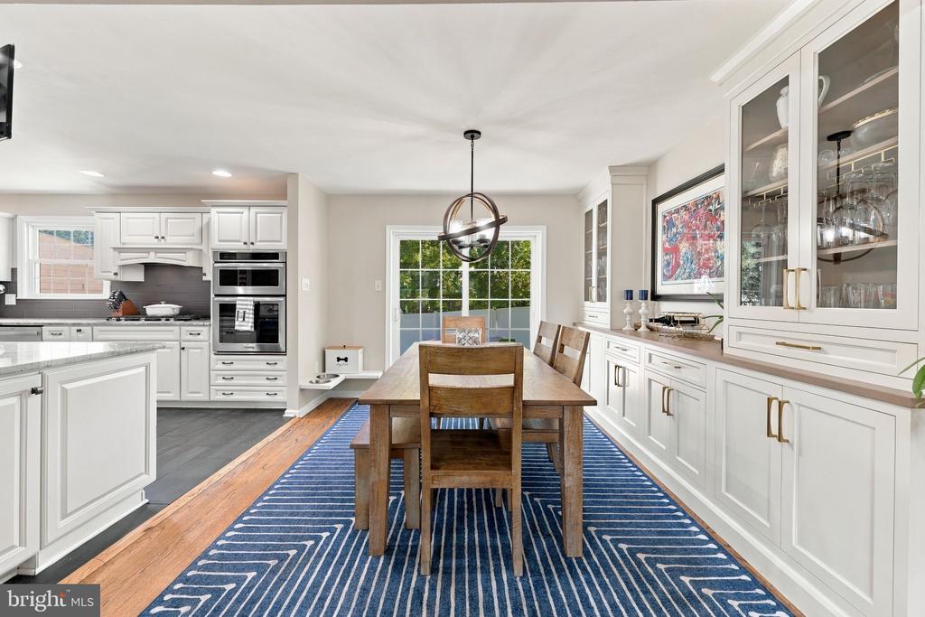 Dining area with a wooden table, blue striped rug, and white cabinetry opening to the kitchen.