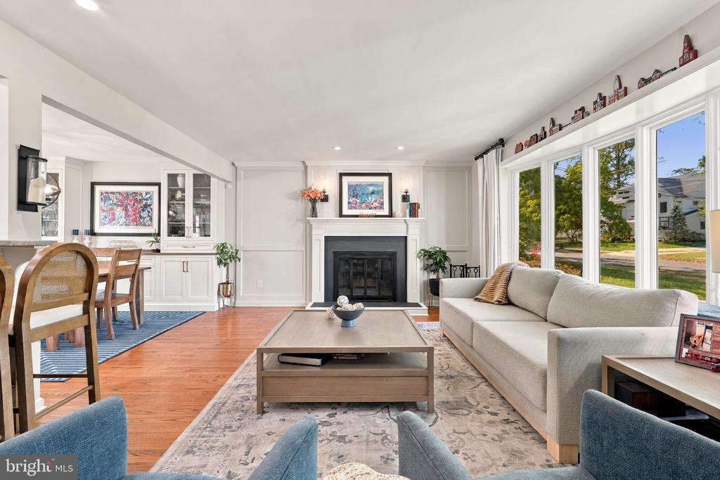 Living room with a fireplace, large windows, hardwood floors, and an adjoining dining area.