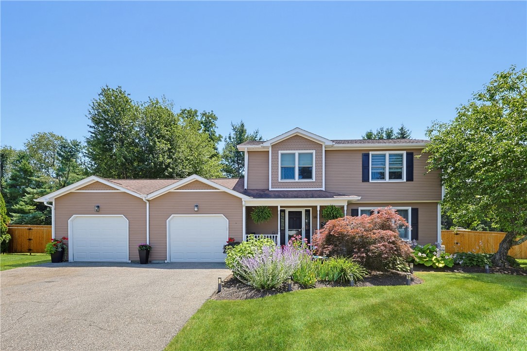 Two-story tan house with a double garage, broad driveway, and colorful front garden.