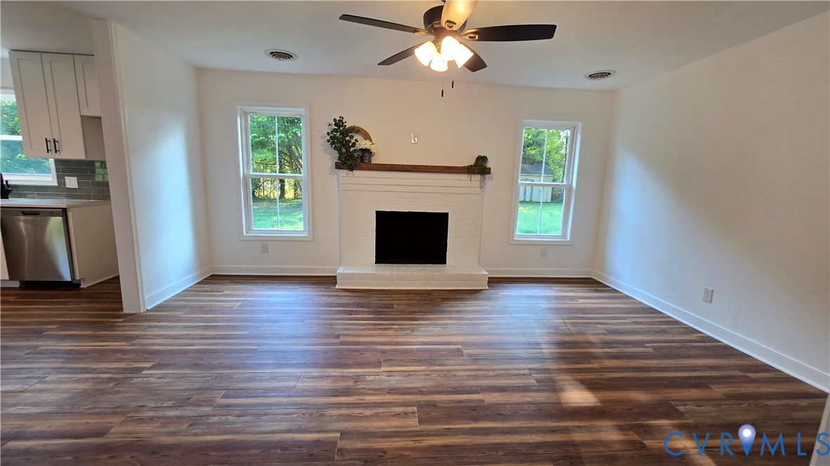 Vacant living room with a white brick fireplace, two windows, and wide wood-look plank flooring.