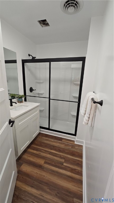 Bathroom with a white vanity, black-framed glass shower doors, and wood-look flooring.