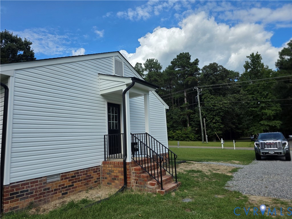 Light-sided home with a brick foundation and covered entry, beside a gravel driveway and parked truck.