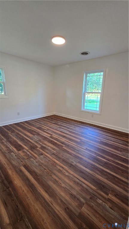 Empty room with dark wood-look flooring and two windows.