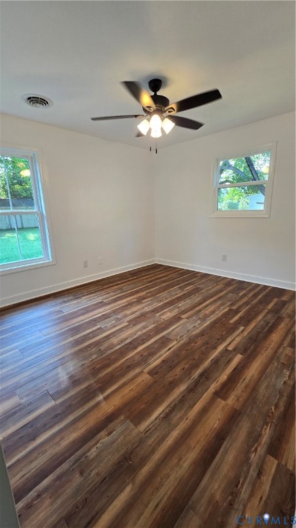 Empty room with dark wood-look flooring, two windows, and a ceiling fan.