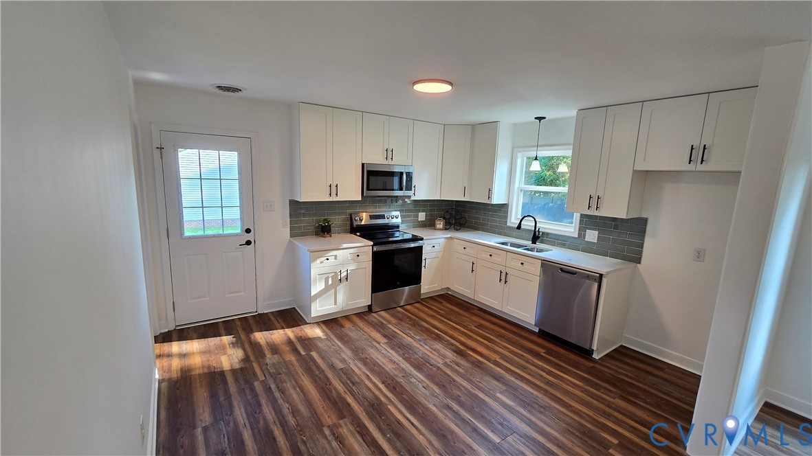 Vacant kitchen with white cabinets, dark tile backsplash, stainless steel appliances, and wood-look flooring.