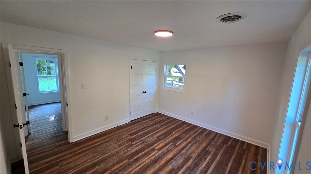 Empty bedroom with dark plank flooring, a double-door closet, and windows.