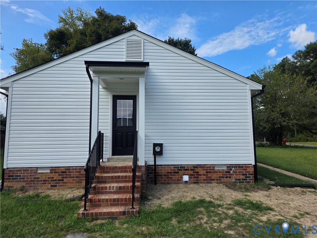 House front with white siding, brick foundation, and a centered entrance above brick steps.
