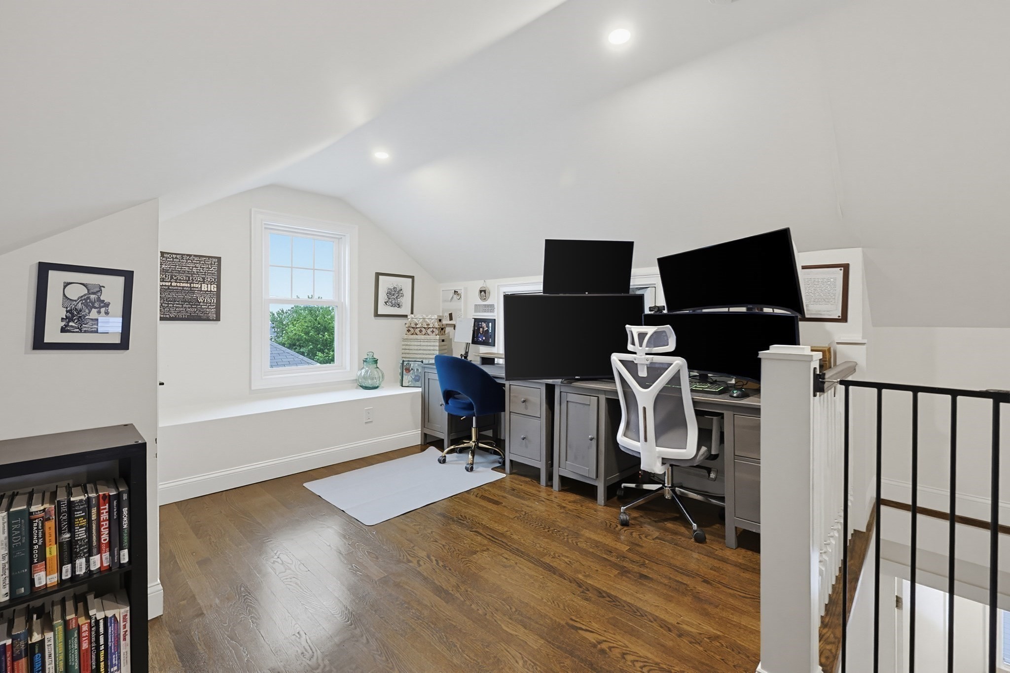 Upper-level home office with a sloped ceiling, hardwood floors, and a desk with multiple monitors.