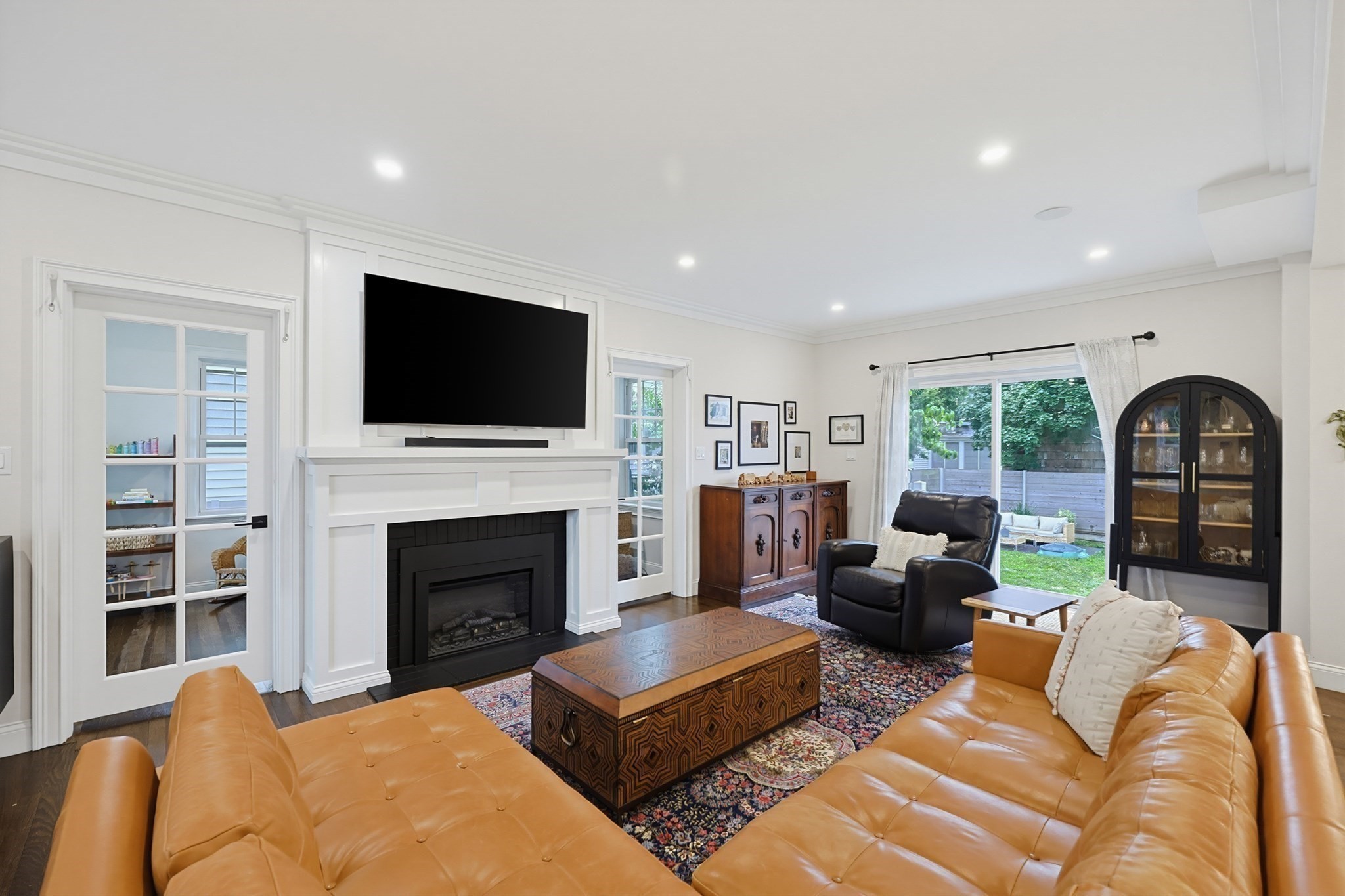 Living room with caramel leather sofas, a white fireplace, and French doors overlooking the backyard.