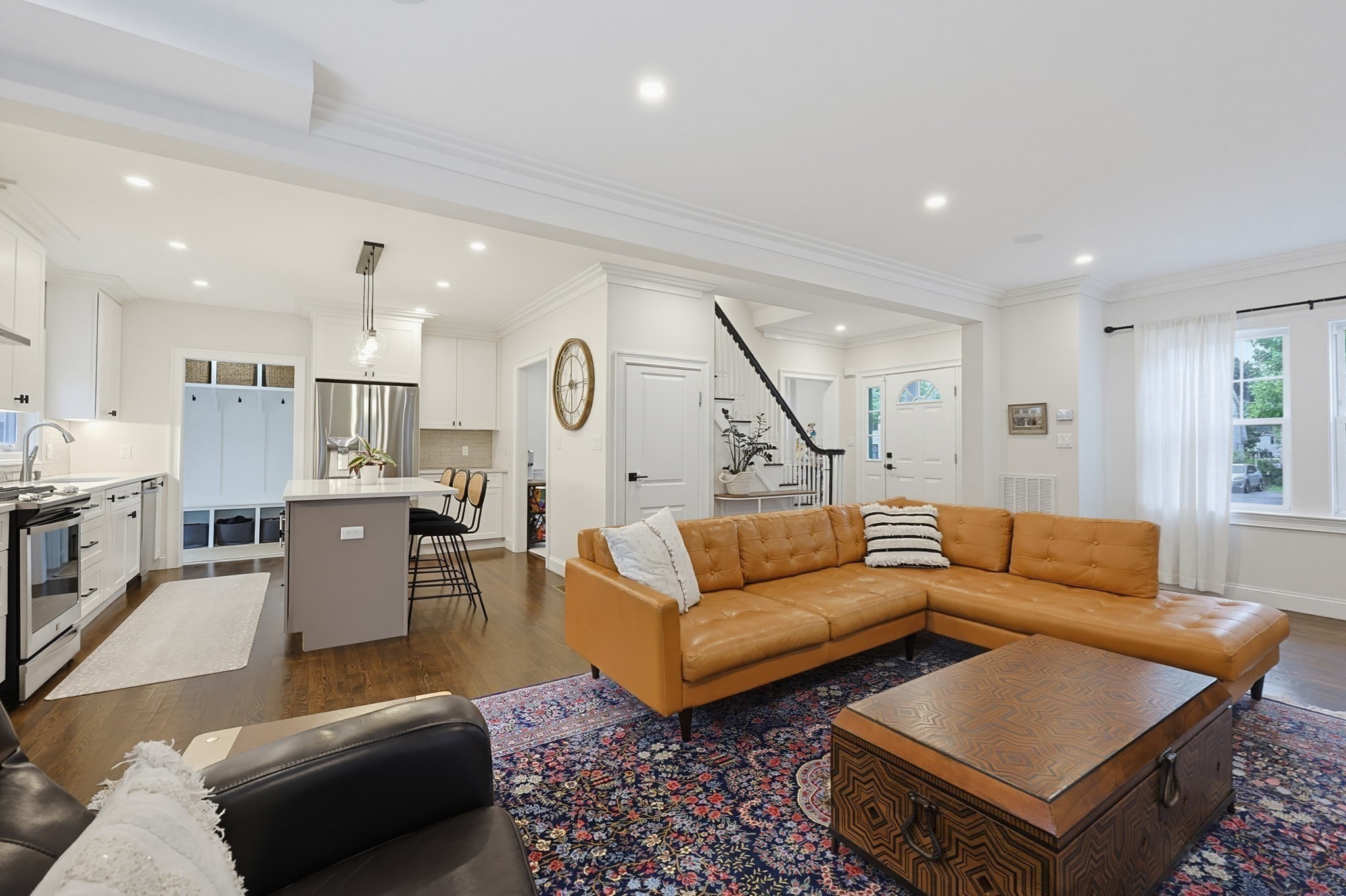 Open-plan living room and kitchen with a tan leather sectional, patterned rug, and white cabinetry.