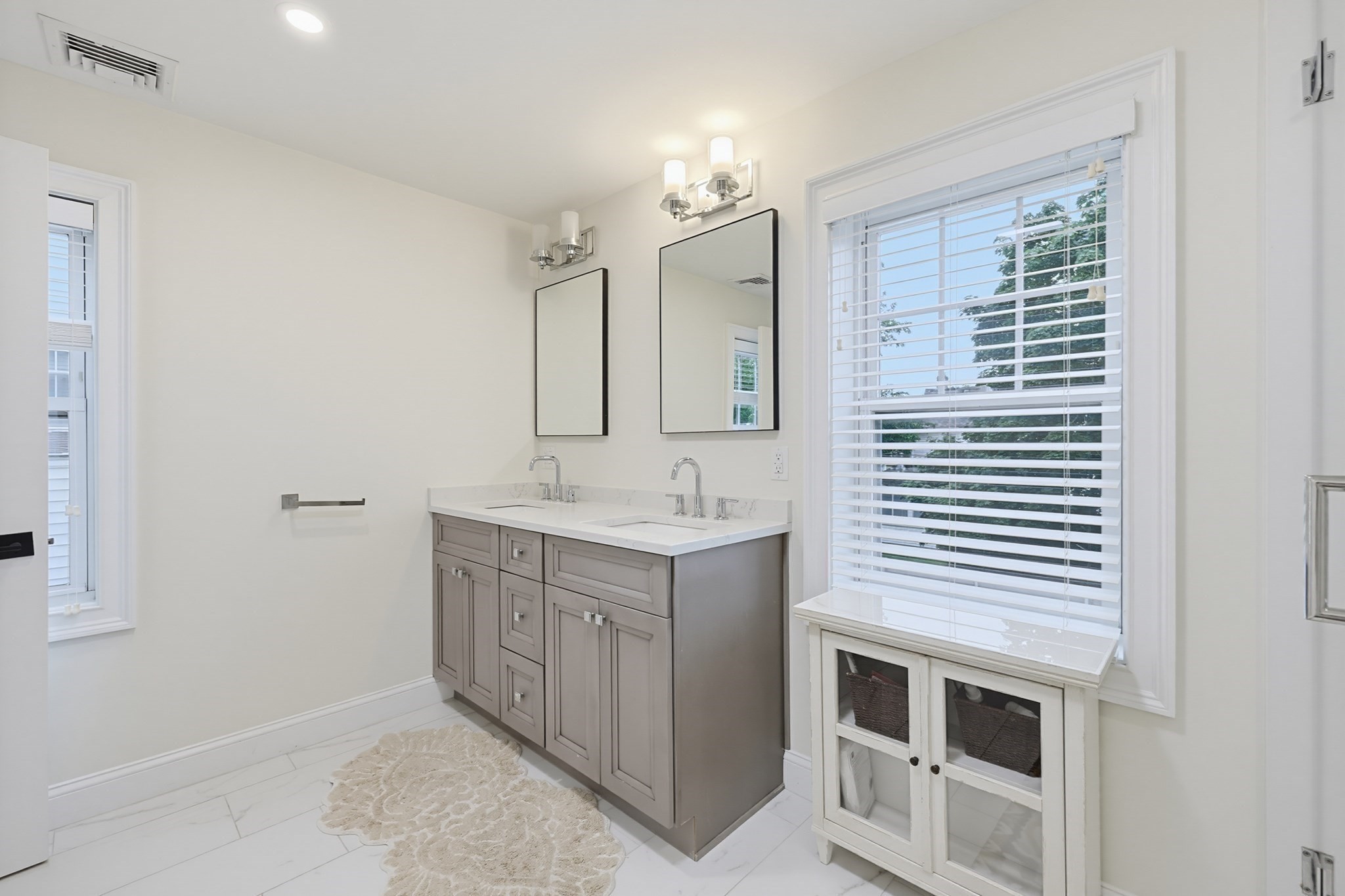 Bathroom with a gray double vanity, large mirrors, and a wide window above a built-in storage bench.