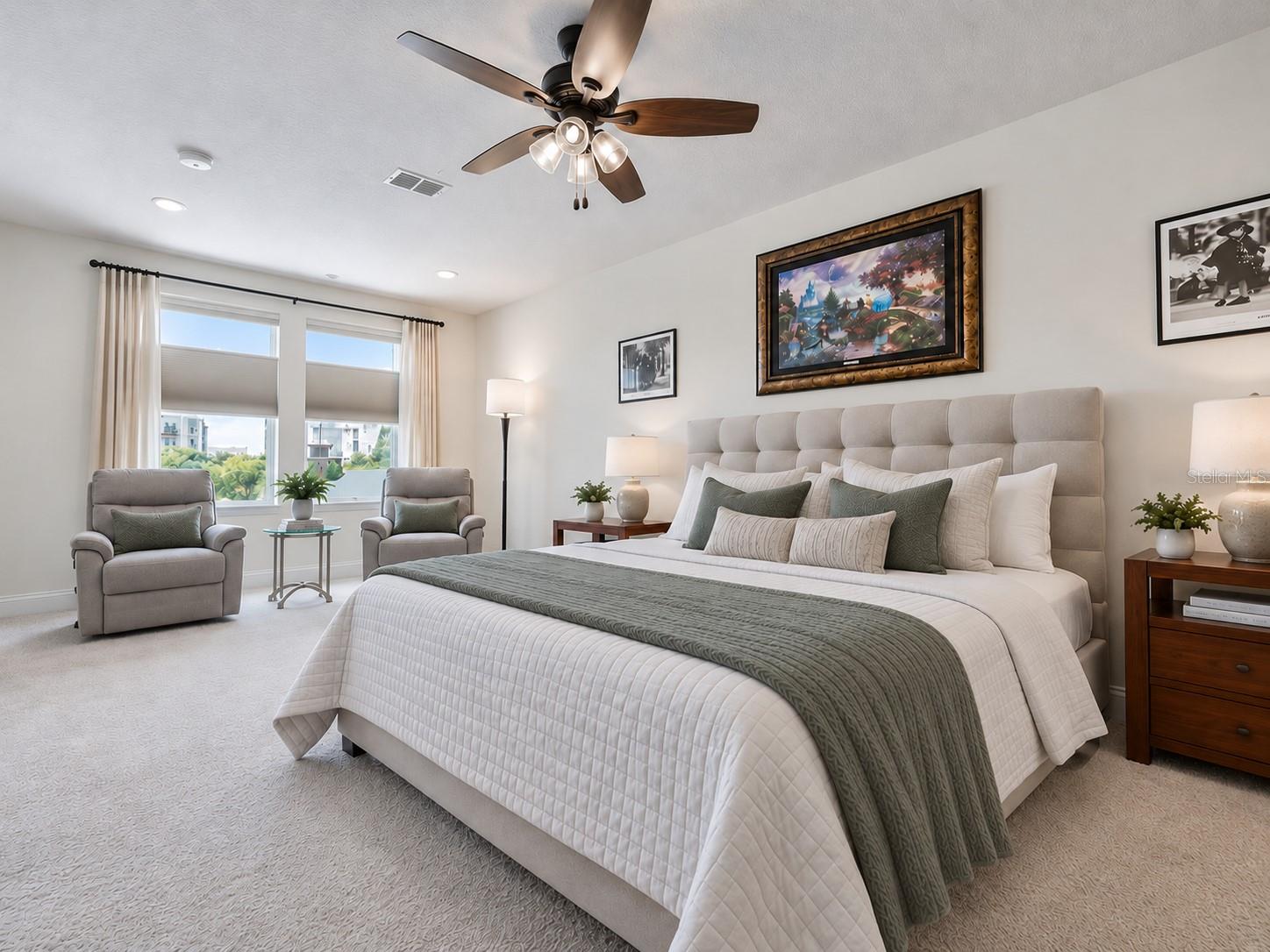 Bedroom with a large white bed, sage-green bedding, and two gray armchairs beside the windows.