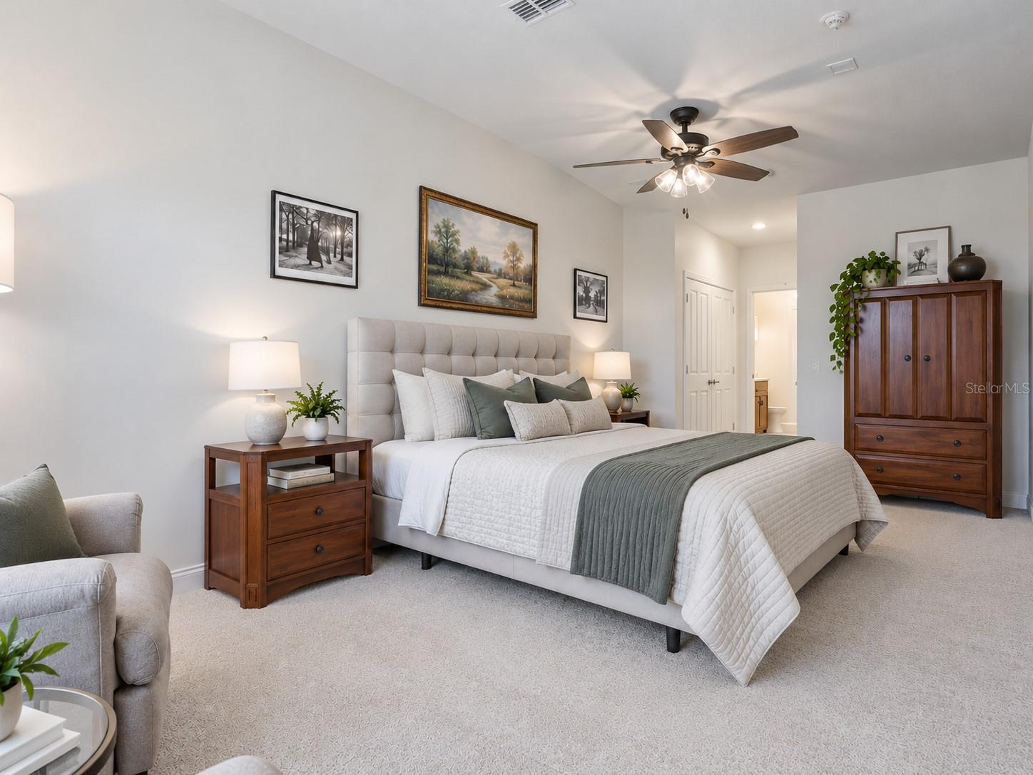Staged bedroom with a tufted headboard, sage-green throw, dark wood furniture, and ceiling fan.