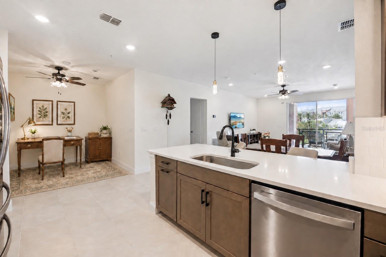 Open-plan kitchen with a large white island, dark wood cabinetry, and dining area beside balcony doors.