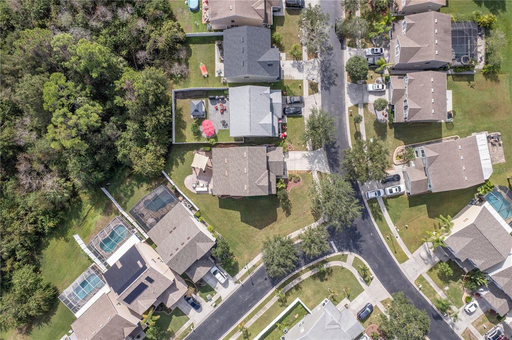 Aerial view of homes beside a wooded area, with a fenced backyard and patio.