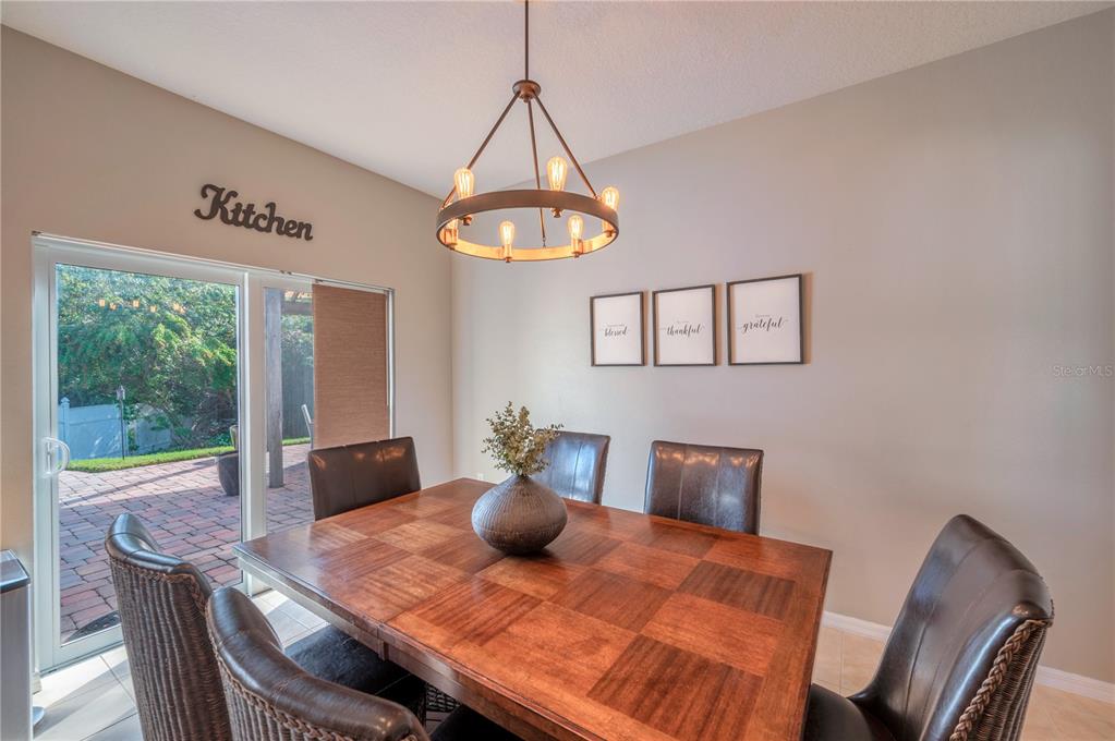 Dining area with a square wood table and leather chairs beside sliding glass doors to a brick patio.