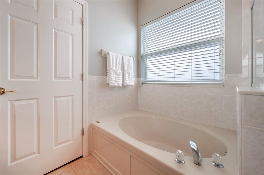 Bathroom with an oval soaking tub beneath a large window with blinds.