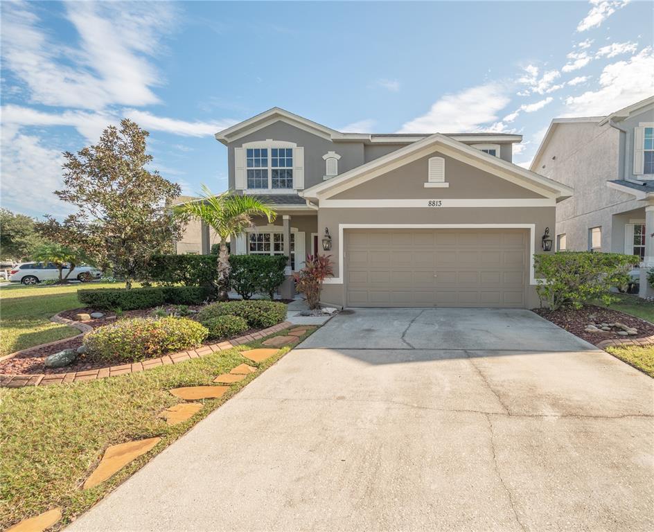 Two-story gray house with a two-car garage, landscaped front yard, and wide concrete driveway.