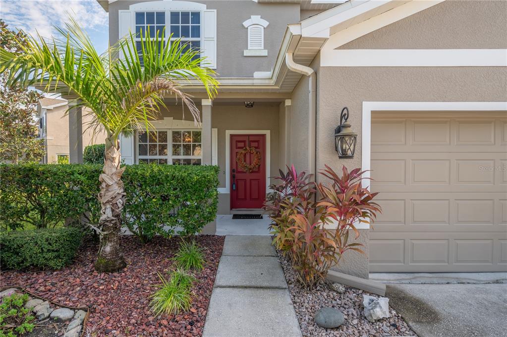 Two-story home with a red front door, attached garage, palm tree, and landscaped entry walkway.