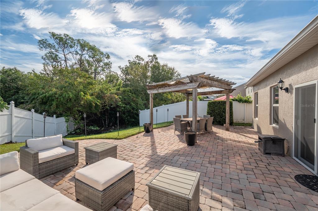 Paved backyard patio with wicker seating and a dining set beneath a wooden pergola.