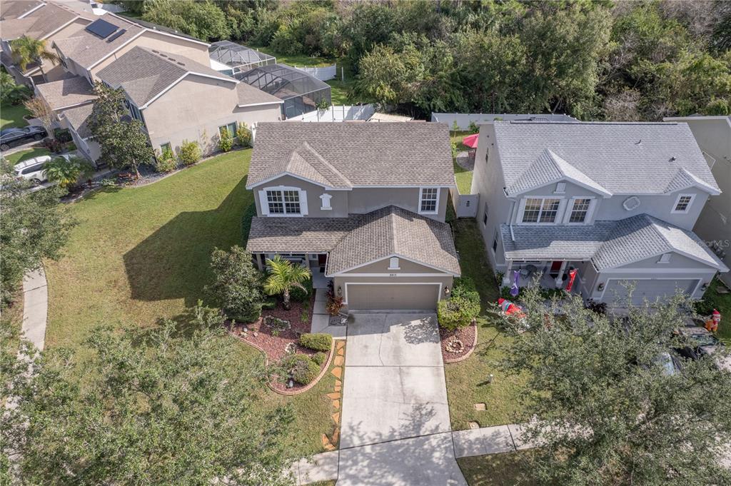 Gray single-story home with an attached garage, curved garden beds, and a long driveway.