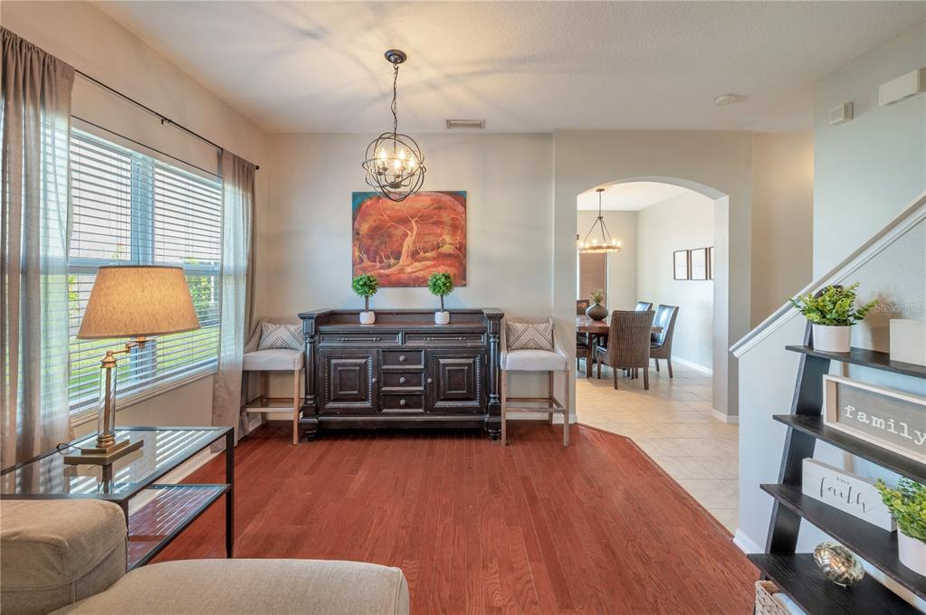 Staged living room with reddish hardwood floors, a dark sideboard, and an arched opening to the dining room.