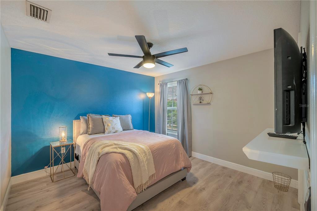 Furnished bedroom with pink bedding, a turquoise accent wall, and a ceiling fan.