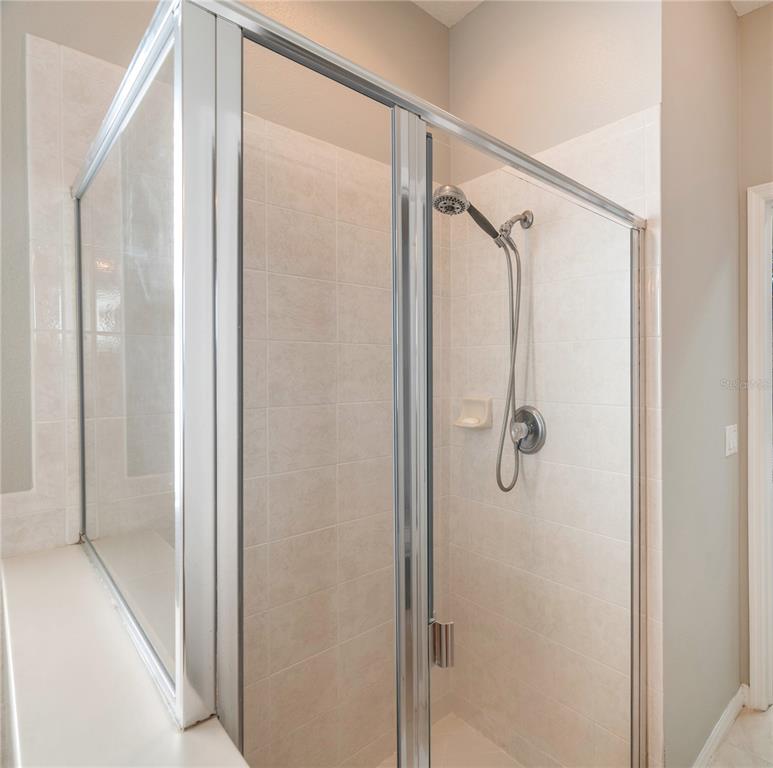 Walk-in tiled shower with a clear glass enclosure and handheld showerhead.