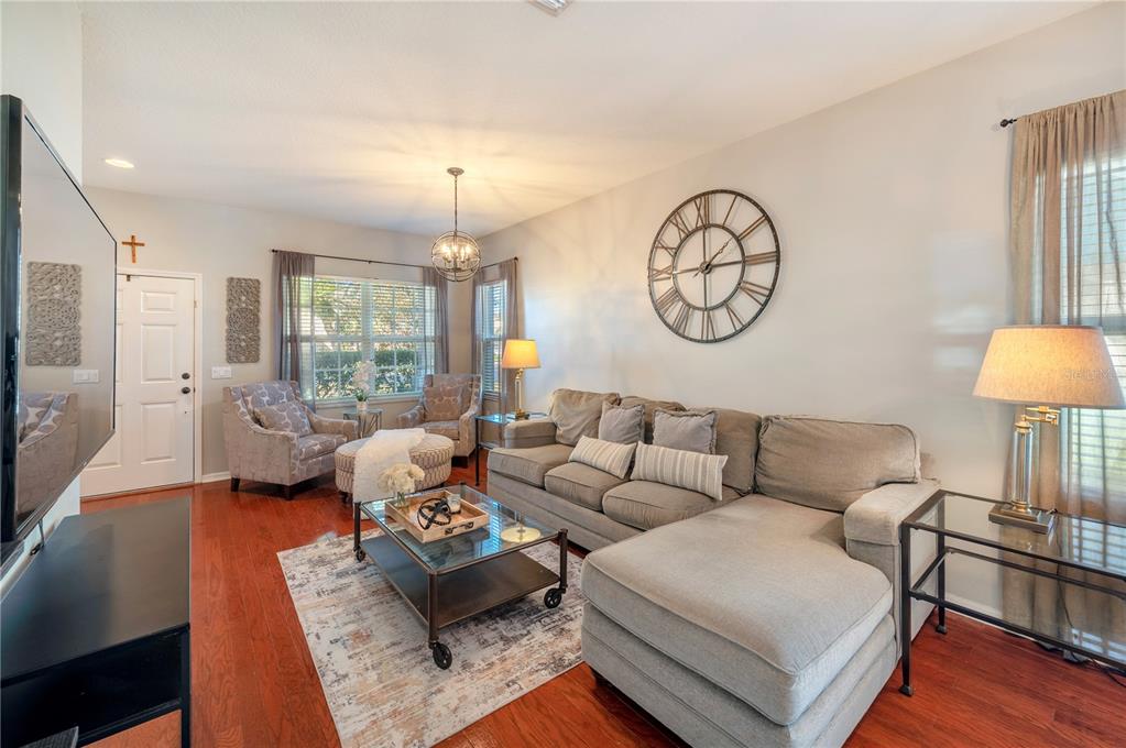 Furnished living room with a gray sectional, glass coffee table, and large curtained windows.
