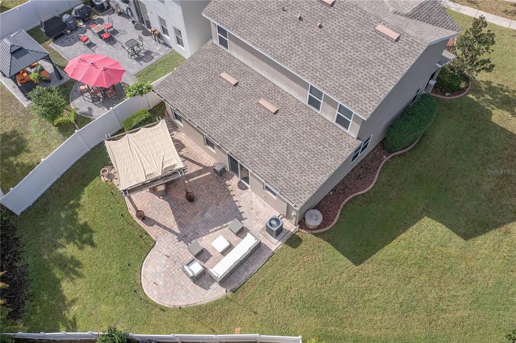 Aerial view of a two-story home and paved backyard patio with a shade canopy and outdoor seating.