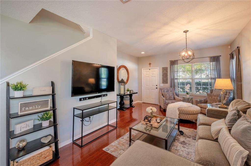 Living room with hardwood floors, wall-mounted television, neutral seating, and a large curtained window.