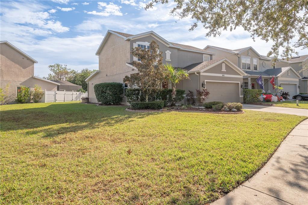 Two-story gray stucco home with an attached garage, landscaped entrance, and broad front lawn.