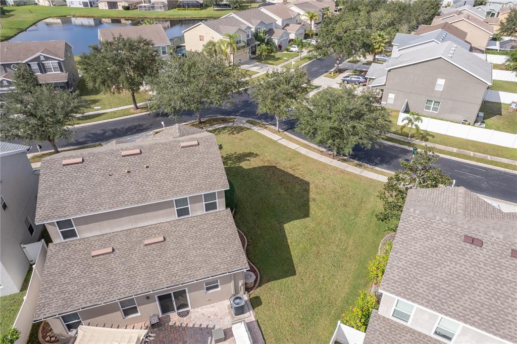 Aerial view of a two-story home and backyard, with a tree-lined street and pond beyond.