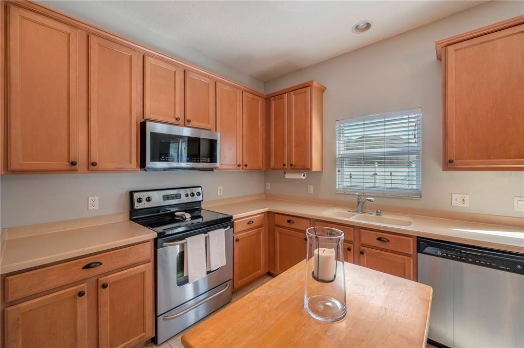 Kitchen with honey-toned wood cabinets, stainless steel appliances, and a sink beneath a window.