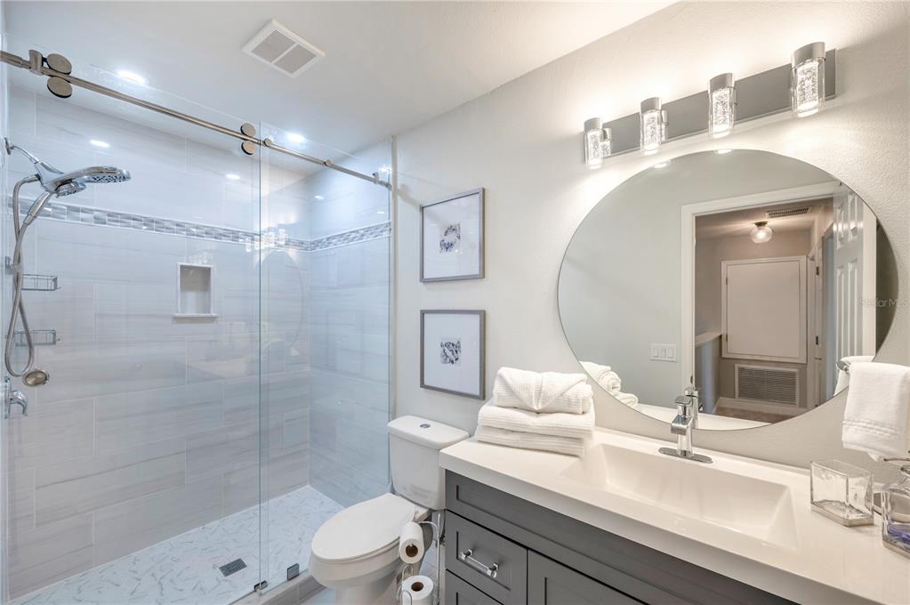 Bathroom with a glass walk-in shower, gray vanity, and large round mirror.