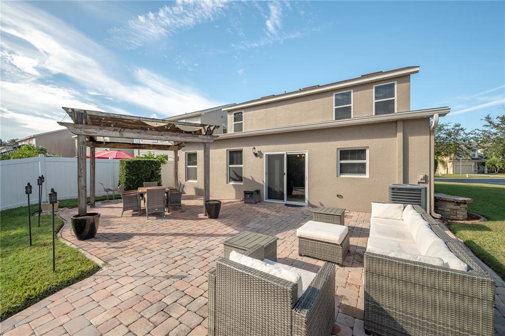 Home’s rear exterior with a paver patio, wooden pergola, and wicker outdoor seating.