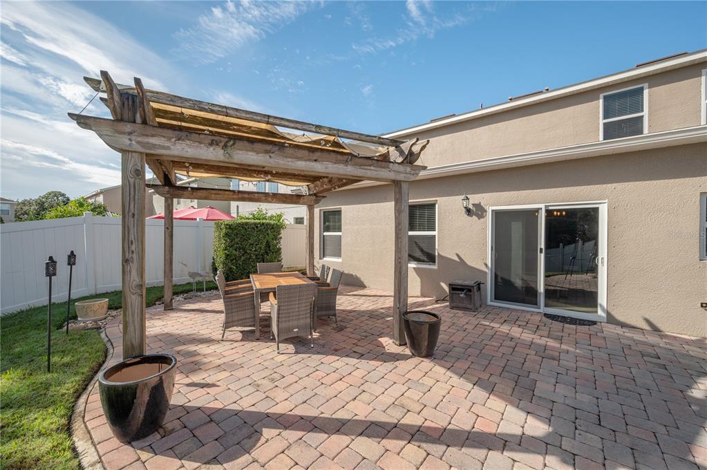 Brick-paver backyard patio with a weathered wooden pergola and outdoor dining set beside the home.