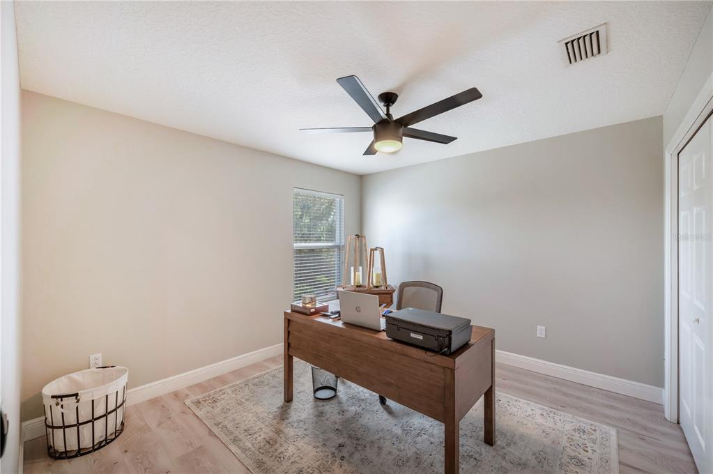 Furnished home office with a wooden desk, laptop, and printer beneath a ceiling fan.