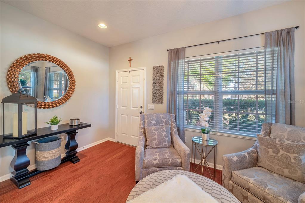 Living room with patterned armchairs, reddish wood flooring, and a wide window overlooking greenery.