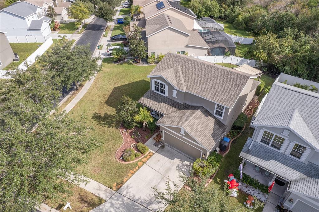 Aerial view of a two-story home with a broad front lawn, landscaped beds, and a concrete driveway.