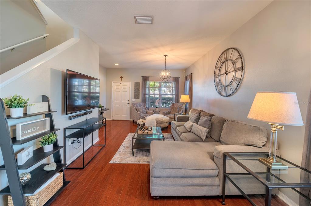 Furnished living room with a gray sectional, wall-mounted TV, and large open-frame wall clock.
